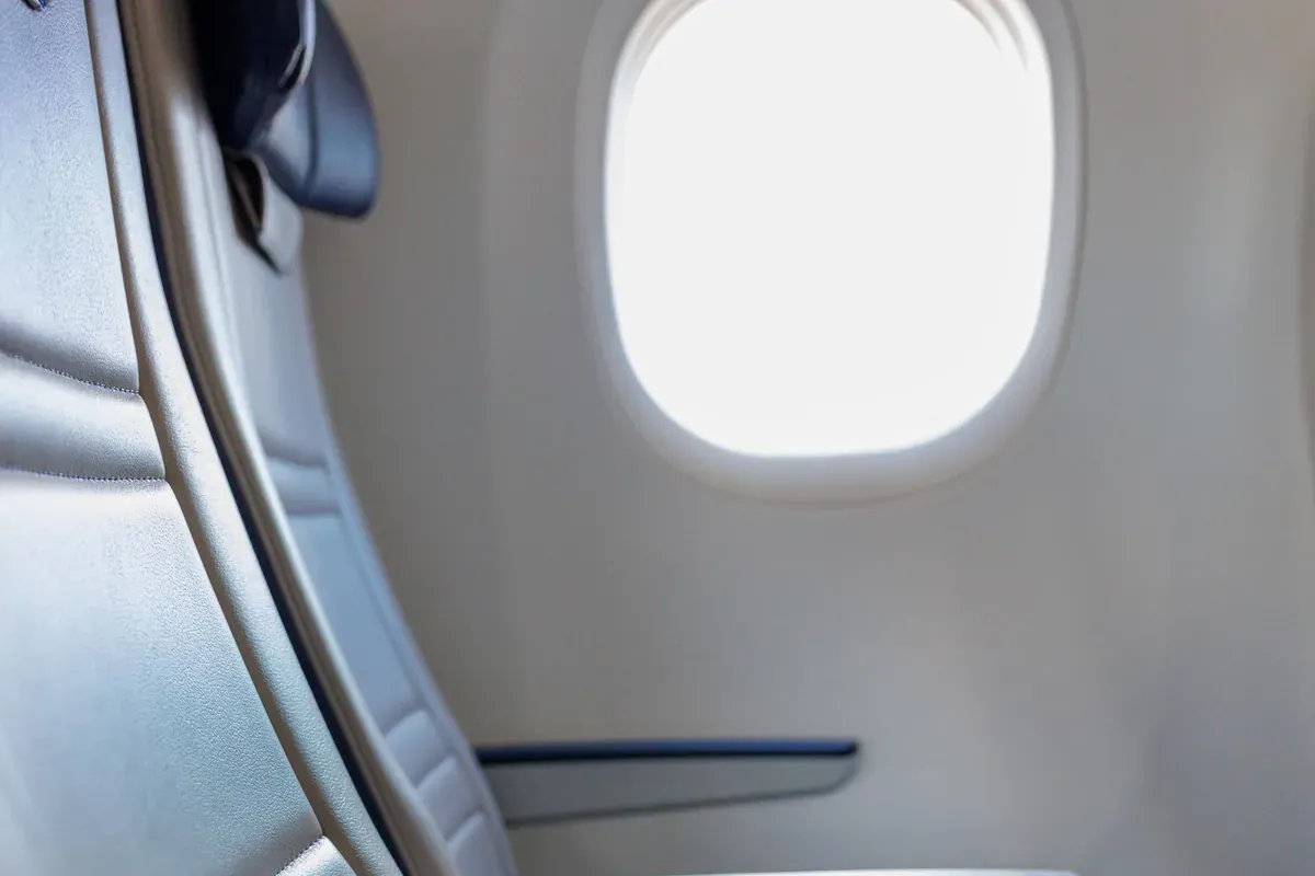 Un asiento de ventanilla de avión con luz de día entrando en la cabina