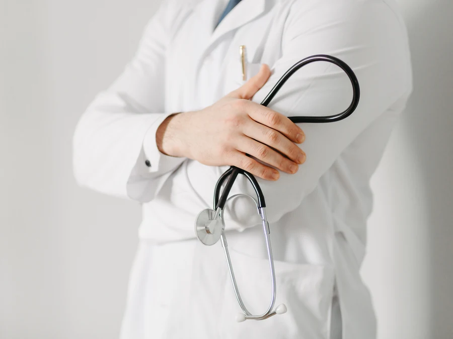 Un médico con bata blanca, de brazos cruzados, sosteniendo un estetoscopio