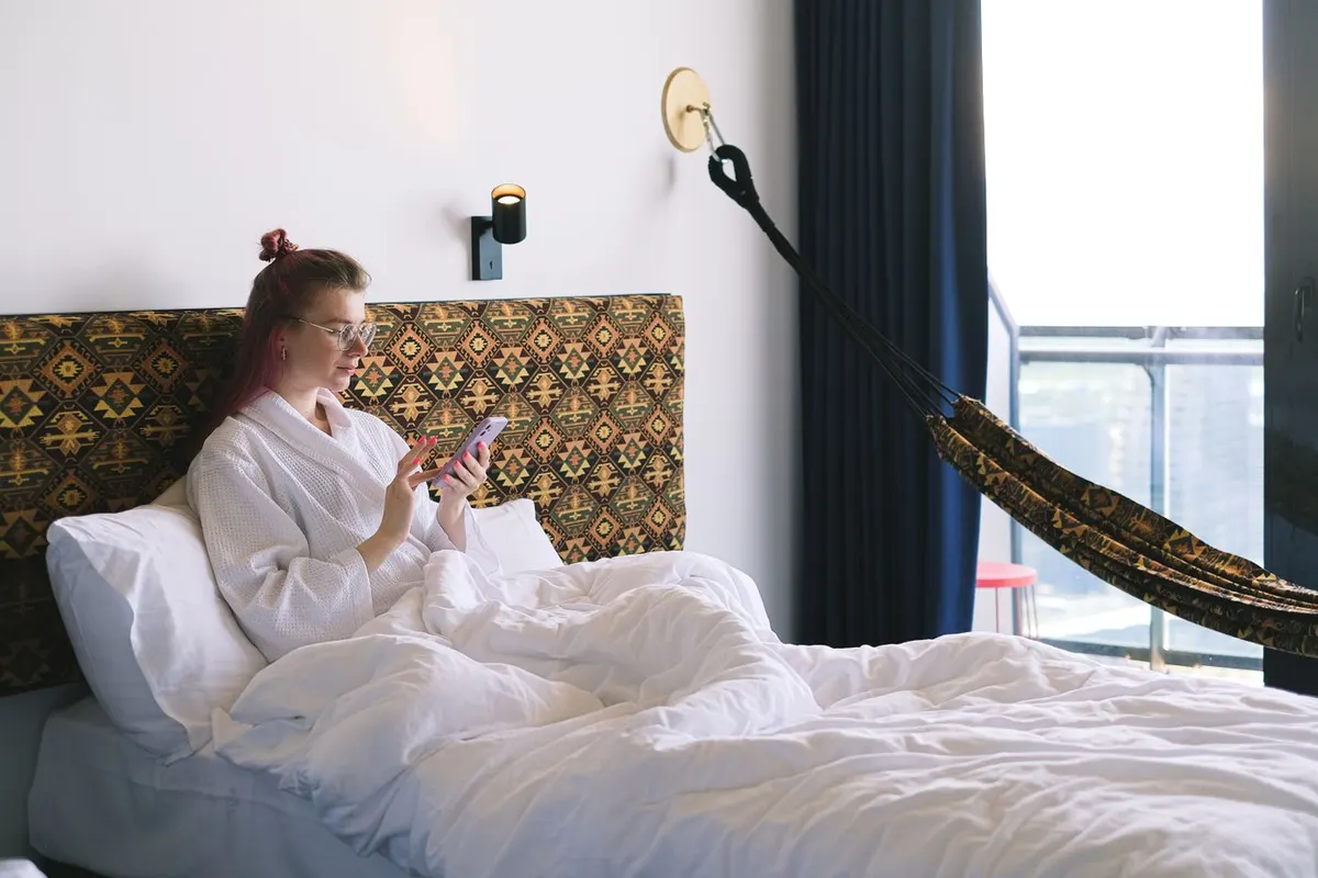 Una viajera consulta su teléfono desde la cama de un hotel