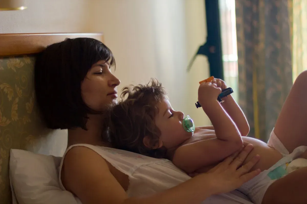 Un adulto tumbado junto a un niño pequeño que descansa en la cama